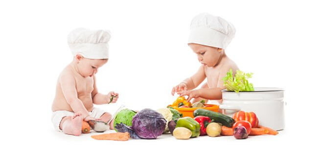 Dois bebes brincando com legumes e frutas 